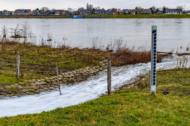 Water flowing into the river Maas, a water level meter, across the river a small Belgian village, cloudy day in Geulle in South Limburg, the Netherlands