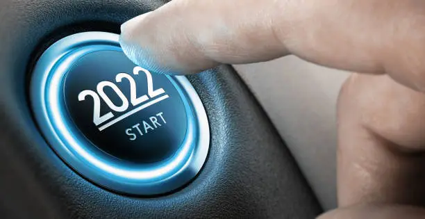 Finger about to press a car ignition button with the text 2022 start. Year two thousand and twenty two concept. Composite image between a hand photography and a 3D background.
