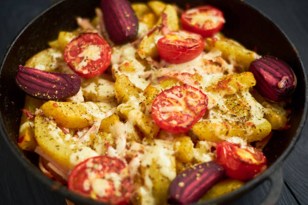 patate cotte, cotte con pomodori, pancetta e formaggio in padella. - potatoes au gratin foto e immagini stock