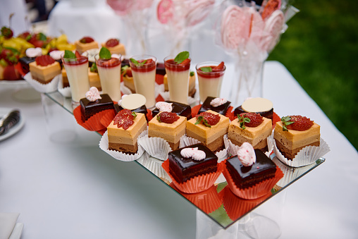 Candy bar served with slices of strawberry and chocolate cake, cream dessert in glasses on table outdoors, copy space. Dessert table for birthday party or wedding reception. Holiday concept