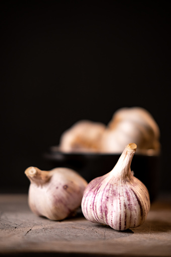 Close up on white garlic on the wooden cutting board. Dark photography style. Place for text above.