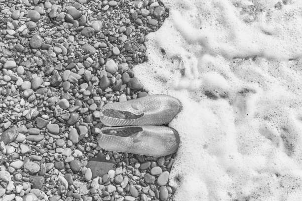 Rubber blue women's slippers for swimming on a pebble beach with sea foap. Top view