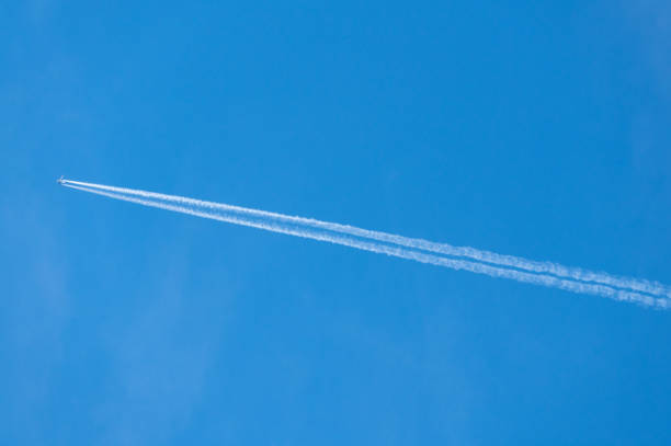 Condensation or contrail behind a two engined jet aircraft flying across blue sky in high definition image