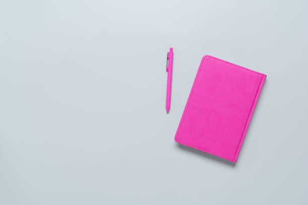 istock Pink notepad and pink ballpoint pen on a gray background. Female workspace. Top view, flat lay. 1310135914