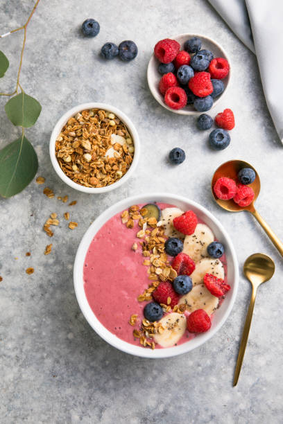 Summer acai smoothie bowls with raspberries, banana, blueberries, and granola on gray concrete background. Breakfast bowl with fruit and cereal, close-up, top view, space for text stock photo