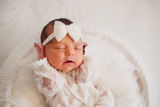 la niña recién nacida duerme en una cesta redonda blanca cubierta con manta de piel; fondo blanco - niñas bebés fotografías e imágenes de stock