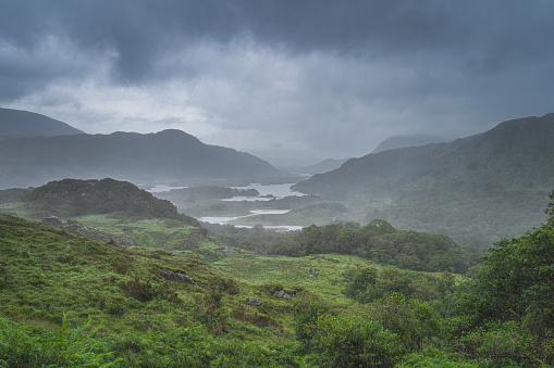 Atmospheric, dramatic storm sky and clouds, mist and heavy rain in Irish iconic viewpoint, Ladies View. Green valley with lake. Rink of Kerry, Ireland