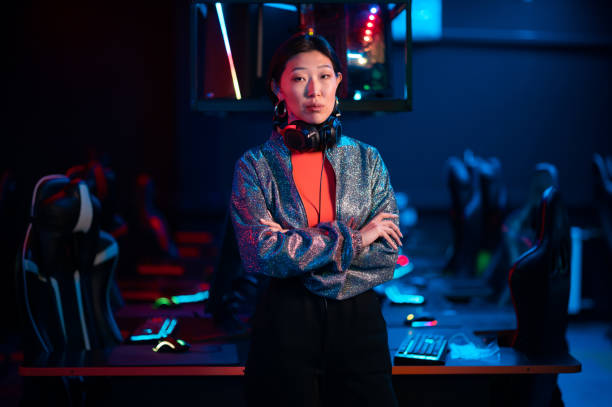 jovem asiático gamer em um fone de ouvido posa para a câmera com os braços cruzados - gaming systems - fotografias e filmes do acervo