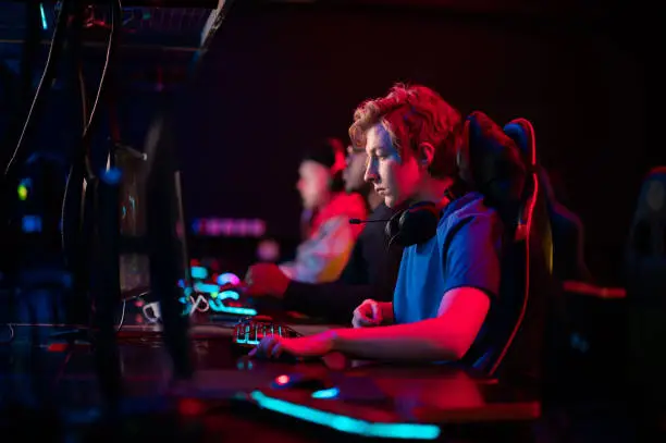 Photo of Training bootcamp for professional esports players. Young cyber-athletes play an online shooter game. Glowing keyboard, neon light