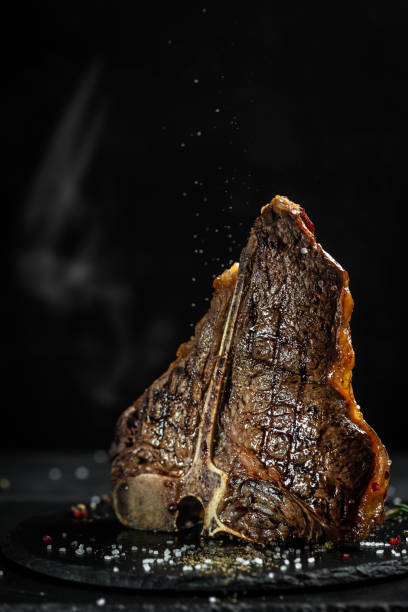 American cuisine. Chef season salt on a juicy beef steak in a restaurant. in a freeze motion on black background. vertical image, place for text American cuisine. Chef season salt on a juicy beef steak in a restaurant. in a freeze motion on black background. vertical image, place for text. steak vertical beef meat stock pictures, royalty-free photos & images