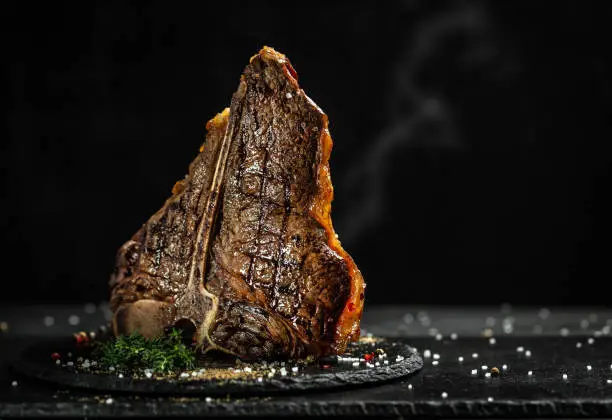 Grilled T-bone steak on stone table. juicy steak rare beef with spices on a black table, banner, menu, recipe, place for text..
