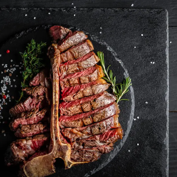 Dry Aged Barbecue Porterhouse Steak T-bone beef steak sliced with large fillet piece with herbs and salt. American meat restaurant. square image, top view.