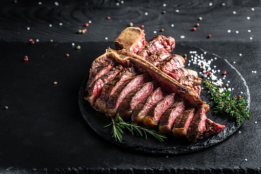 Beef T-Bone steak or aged wagyu porterhouse grilled beef steak Medium rare on a black table. American meat restaurant. menu, recipe, place for text.