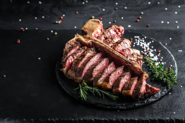 Photo of Beef T-Bone steak or aged wagyu porterhouse grilled beef steak Medium rare on a black table. American meat restaurant. menu, recipe, place for text