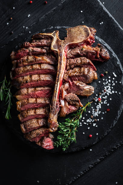 istock Steak on the bone. Grilled beef steak with rosemary, salt and pepper. Top view. vertical image, place for text 1310148585