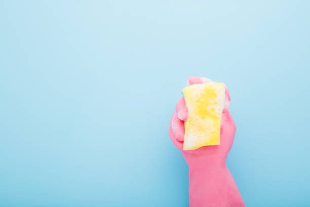 istock Hand in rubber protective glove holding foamy yellow sponge on light blue table background. Pastel color. Empty place for text. Top down view. Closeup. 1310153280