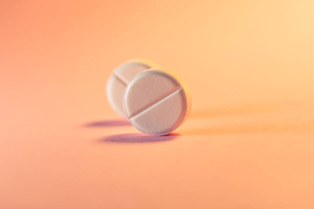 dos pastillas en un fondo rosa anaranjado. tema médico. enfoque selectivo. - pills fotografías e imágenes de stock