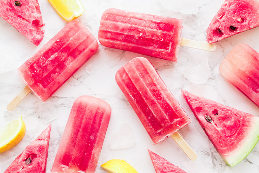 Homemade watermelon popsicles with ice against white marble background. Popsicles from frozen watermelon. Summer concept. Top view.