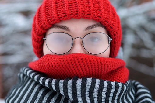 Portrait of a young woman in misted glasses outdoors on a frosty snowy day, camera zoom out