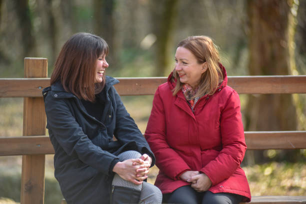 istock Two friends sitting at park bench and smiling and laughing 1310159724