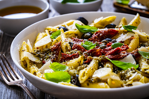 Penne with basil pesto sauce, sun-dried tomatoes, caper and parmesan on wooden table