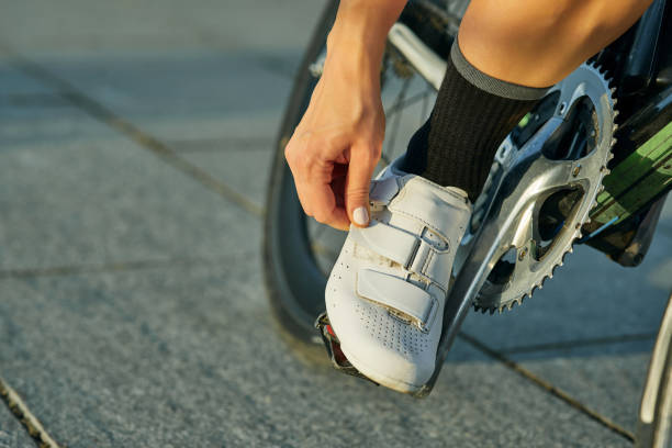 tiro de perto de ciclista feminina vestindo, apertando sapatos de bicicleta enquanto andava de bicicleta, treinando ao ar livre em um dia quente - pedal bicycle sports training cycling - fotografias e filmes do acervo