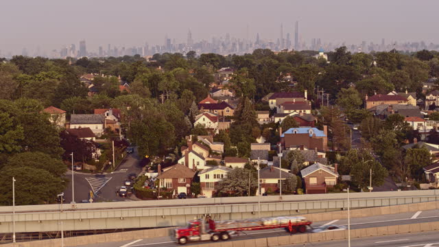 Aerial view of Beechhurst residential neighborhood in Queens with the remote view of Manhattan in the backdrop over Throgs Neck Bridge at sunrise. Drone video footage with the descending camera motion
