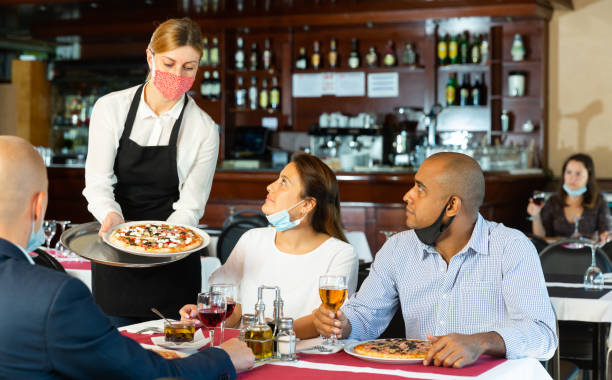 istock Waitress in mask serving cheerful people in pizzeria 1310164702