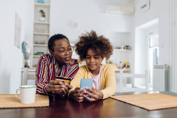 femme aînée afro-américaine et sa petite-fille faisant un achat en ligne à la maison - comptes épargne photos et images de collection