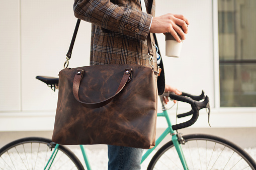 Close-up of an unrecognizable stylish businessman with a cup of coffee going to work by bike.