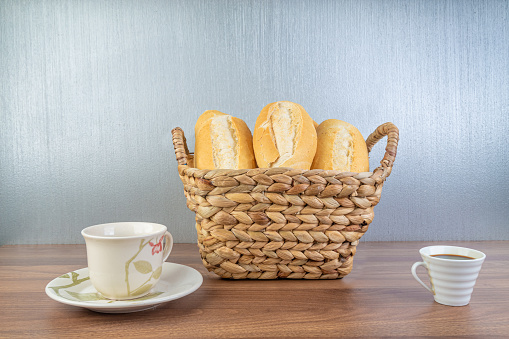 Brazilian Wheat Baked French Bread and coffee, in straw basket on wooden table and gray background - front view.