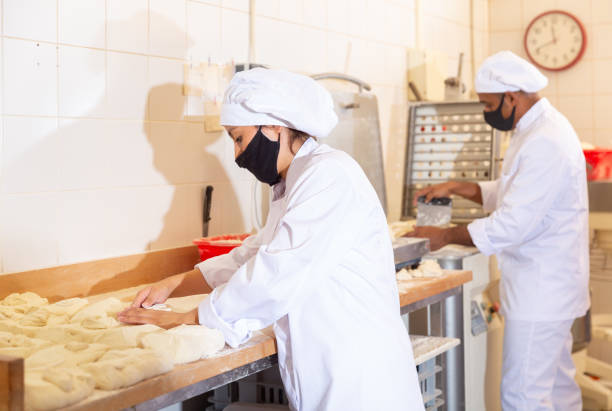 istock Female bakery worker wearing protective mask cuts dough with knife into identical loaves in kitchen 1310180680