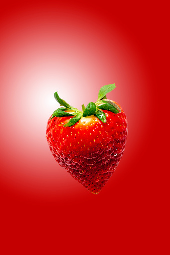 isolated heart shaped strawberry with green leaf and red background. Copy space.