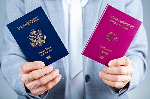 A woman in formal clothes is holding Turkish and US passports. Concept image for immigration to USA, path to citizenship, dual citizen, living abroad and application process for being a US citizen.