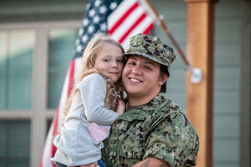 Mother holds elementary age daughter in front yard after arriving home from deployment