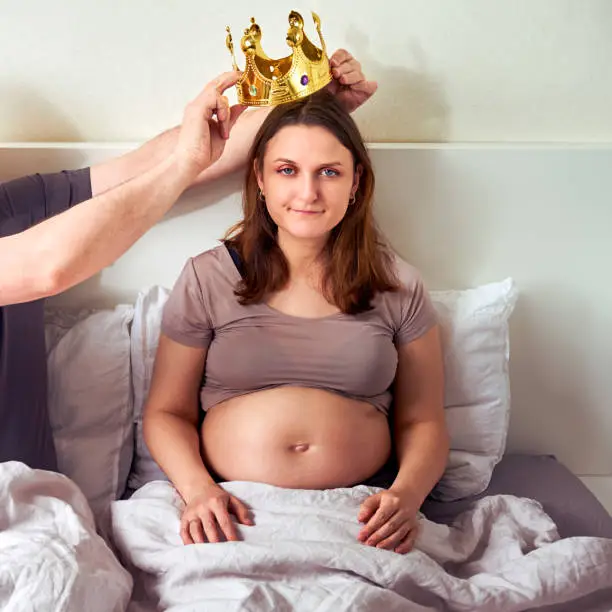 Photo of A man puts a crown on a pregnant woman. Husband and wife with a coronet on their head