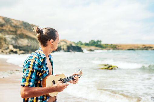 Young man playing on a ukulele guitar by the sea