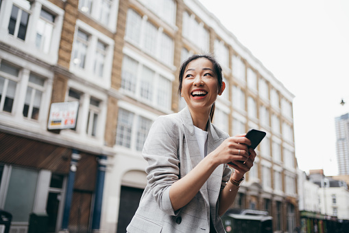 Asian business woman looking far away while using her smartphone on the street of London.