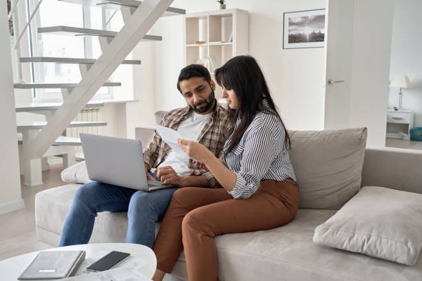 giovane coppia indiana che controlla le bollette cartacee pagando il debito bancario del mutuo ipotecario online insieme al computer, calcolando tasse, spese, effettuando pagamenti, pianificando le finanze del budget familiare usando laptop a casa. - wife husband discussion couple foto e immagini stock