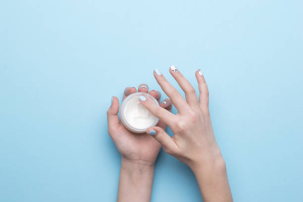 istock Women's hands take cream from a jar on a blue background. Flat lay. 1310199077