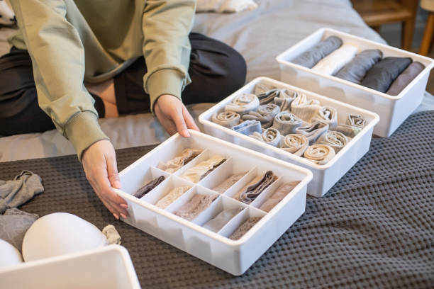 Osoba układa bieliznę w neutralnych kolorach w pudełkach do przechowywania na łóżku, podkreślając wybór materiałów zapewniających zdrowie skóry.