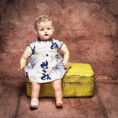 A vintage doll from 1950s sitting in front of a yellow toolbox.