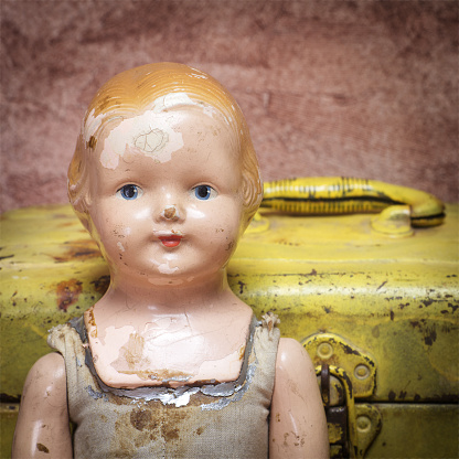 A vintage doll from 1950s sitting in front of a yellow toolbox.