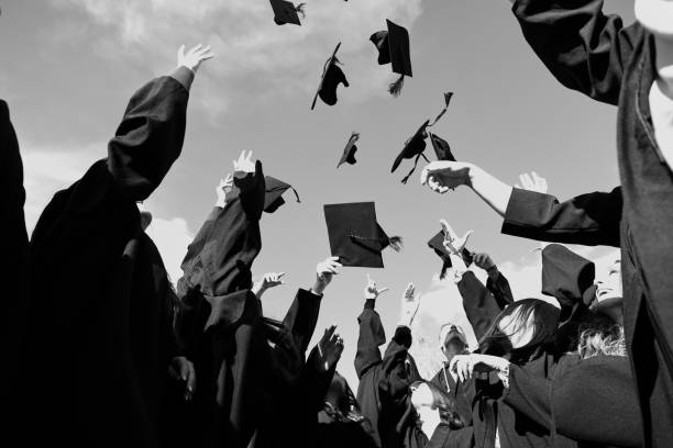 Congratulations Low angle view of happy group of six young cheerful graduates in black gowns, throwing up their head wear in the air and celebrating, in blue summer sky, laughing, enjoying