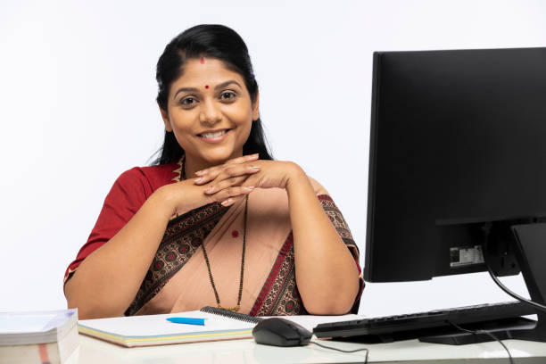 Portrait of Indian woman as a teacher in sari using computer sitting isolated over white background:- stock photo Adult, adult only, teacher using computer,  India, Indian ethnicity, indian teacher stock pictures, royalty-free photos & images