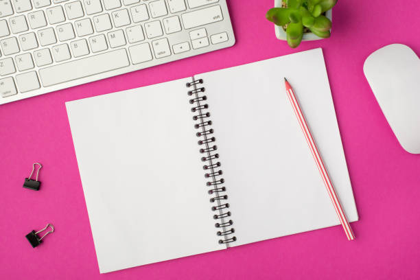istock Top view photo of workplace with white keyboard mouse binders plant pencil on open notebook on isolated pink background with copyspace 1310212305