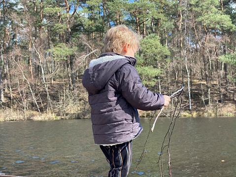 Toddler boy fishing and playing near the water on a weekend day