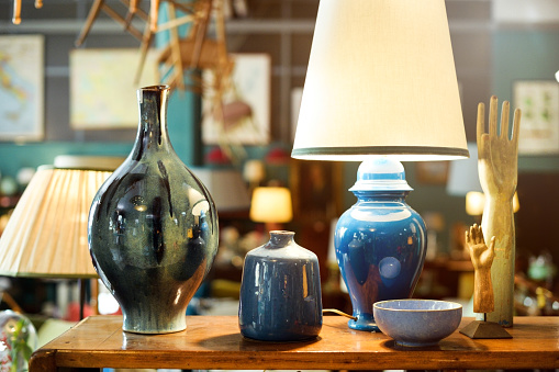 Display of handmade colorful glazed pottery or ceramics in a store with a table lamp, vases, bowl, hands on stands and jar in a shop interior