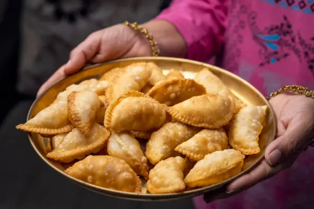 woman holding a plate full of gujia or karanji, an Indian famous snack especially made during the Holi festival of colors.
