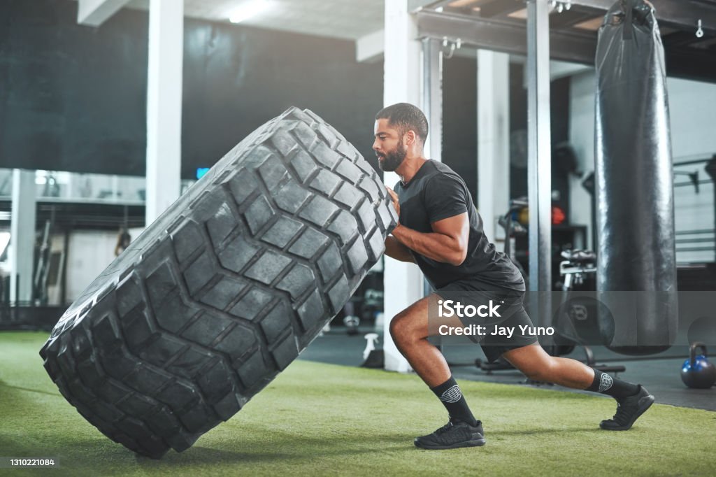 It's okay to struggle - it's not okay to give up Shot of a young man flipping a heavy tyre in a gym Tire - Vehicle Part Stock Photo